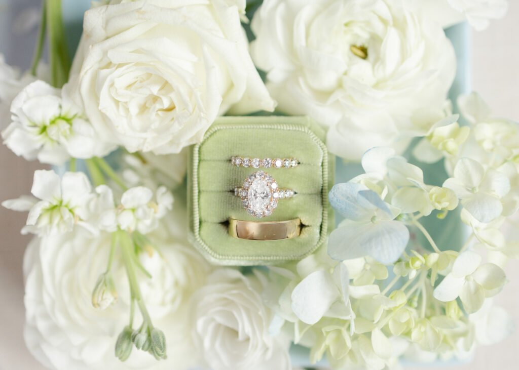 Wedding rings in a green velvet ring box surrounded by white flowers