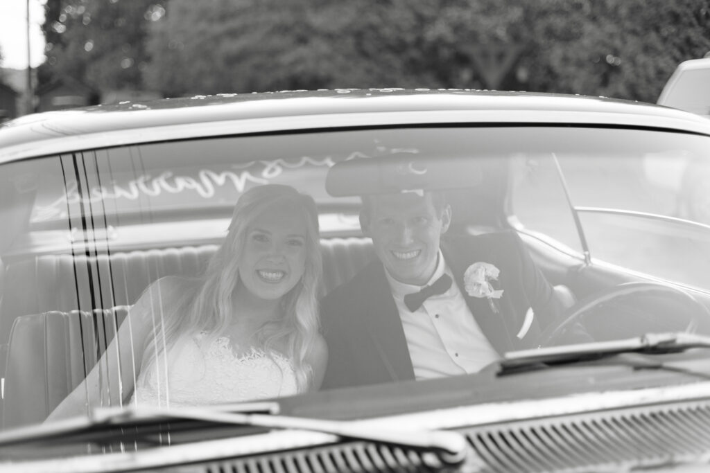 Taylor and Alex sitting together in Alex’s red getaway car after their wedding