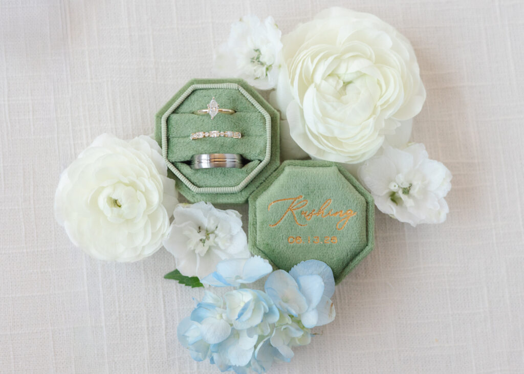 Wedding rings in a green velvet ring box surrounded by white flowers